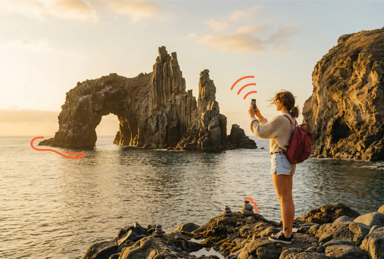 Voyageuse photographiant une arche rocheuse en bord de mer avec son téléphone, surmonté d’un symbole Wi-Fi